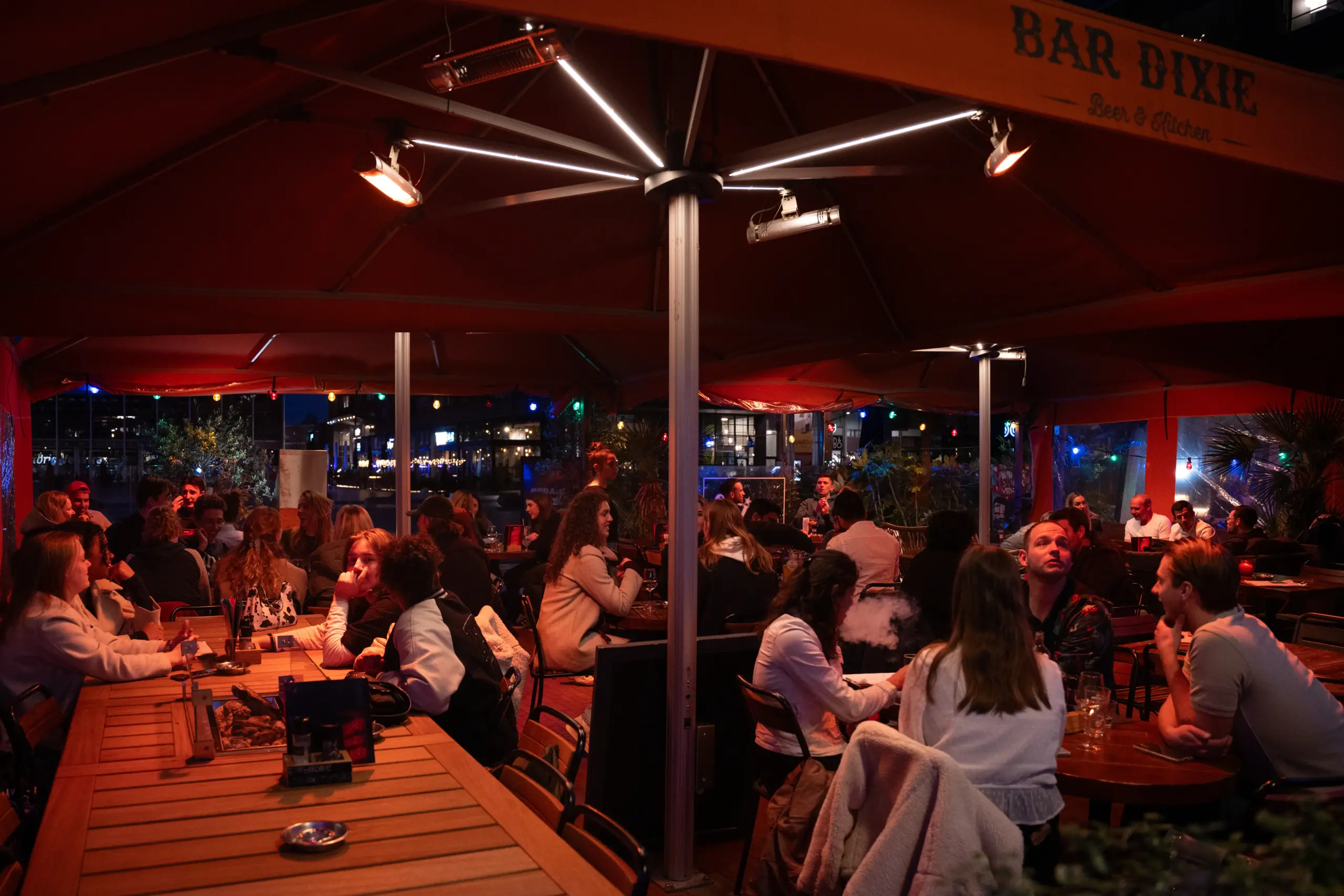 Gezellig verlicht terras van Bar Dixie Amstelveen in de avond met gasten die cocktails drinken